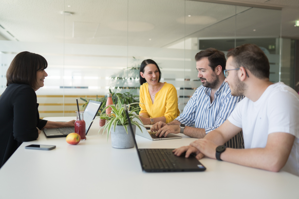 Un gruppo di persone collabora attorno a un tavolo, discutendo e lavorando su laptop.