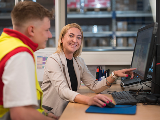 Un uomo e una donna conversano davanti a computer in un magazzino.
