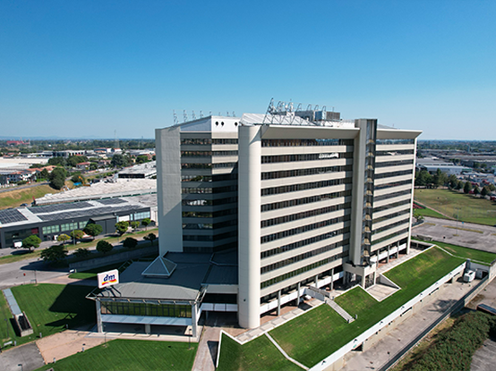 Una vista aerea di un grande edificio moderno, con il logo di dm ben visibile, circondato da spazi verdi e parcheggi.